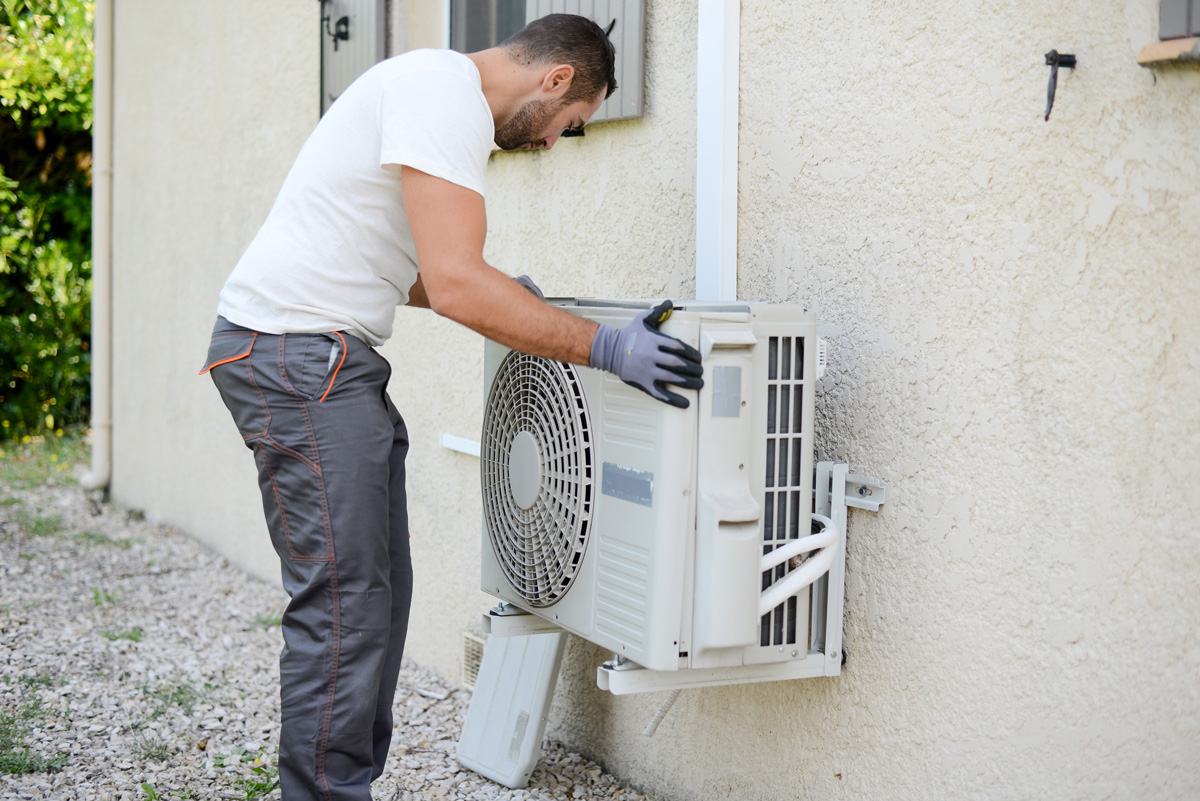 A man in grey pants installing an outdoor AC unit in El Paso.