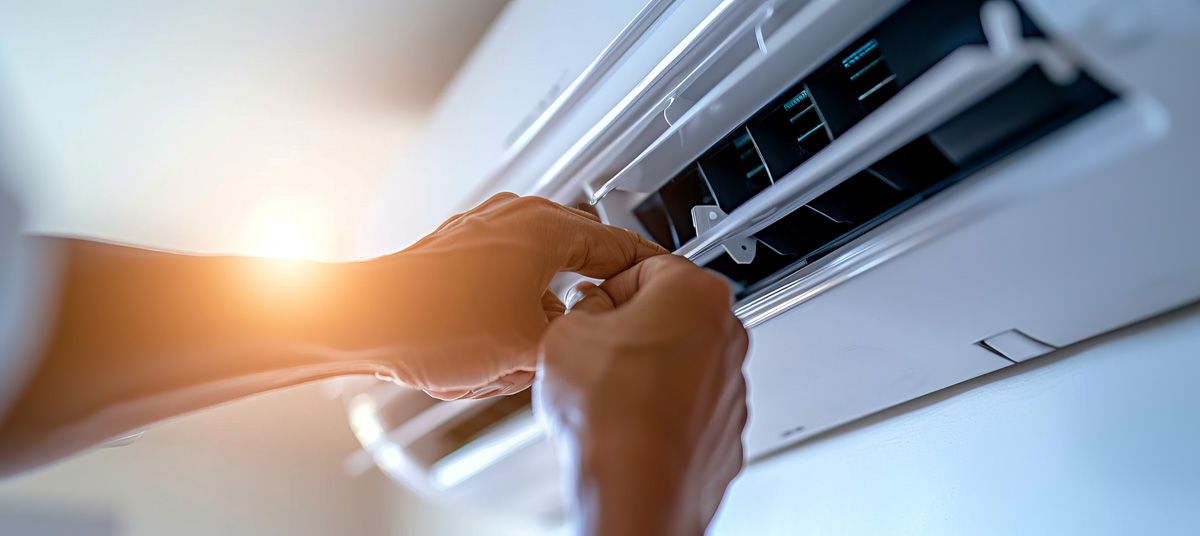 A person’s hands fixing a wall AC unit.